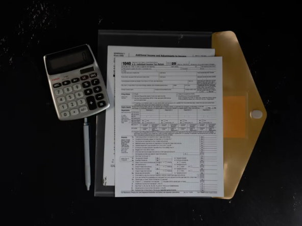 US tax forms in a folder beside a calculator and pen on a dark desk.