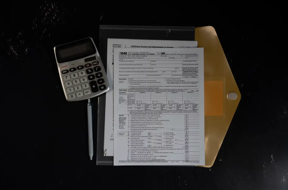 US tax forms in a folder beside a calculator and pen on a dark desk.